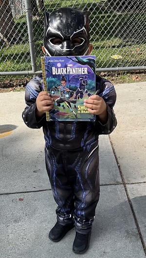 Politi 2nd grader in a Black Panther custume holding his new Black Panther book he received