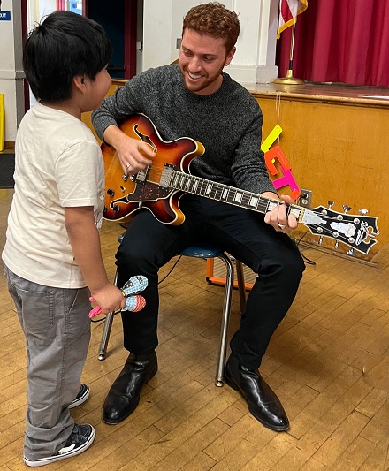 Atticus sharing his guitar with a kid at Tenth St. Elementary