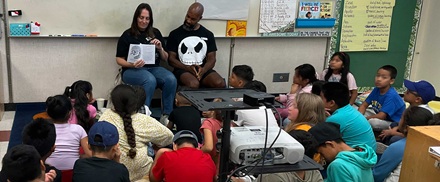 Two volunteers read to a large group at Gratts