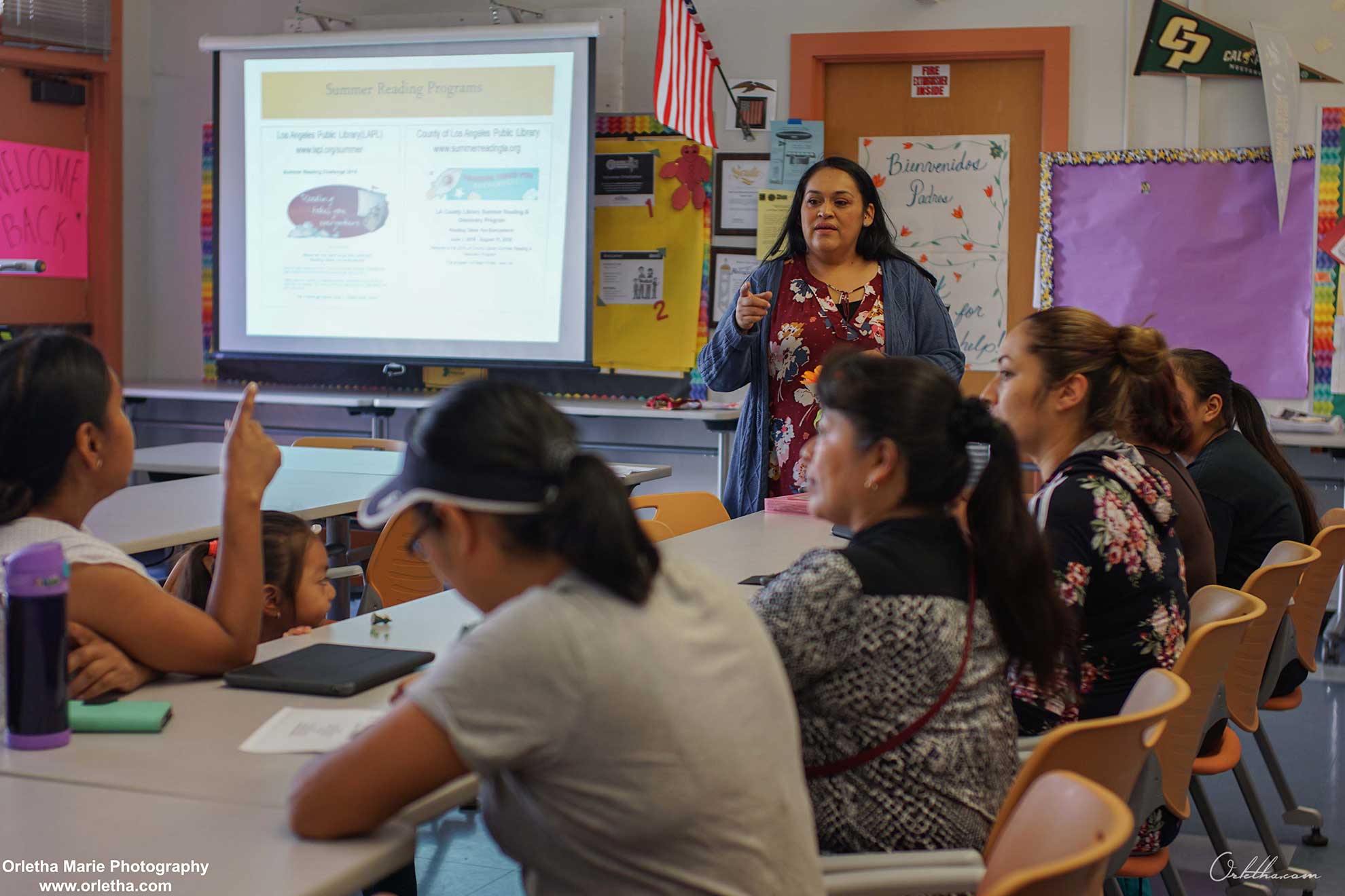 Una sesión de taller para padres en la Escuela Primaria Alta Loma, con padres sentados en una mesa escuchando a una profesora.